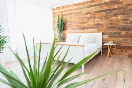 Comfortable boho interior style bedroom. Big bed , green flowers and wooden wall.の写真素材