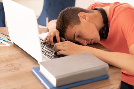 Teenage boy doing homework using computer sitting by desk in room alone.