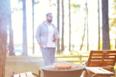Man standing with beer, cooking meat on a barbecue grill at outdoor summer party.の写真素材