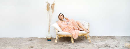 Summer travel vacation relaxation concept. An attractive blonde woman sitting on a boho sofa on a...