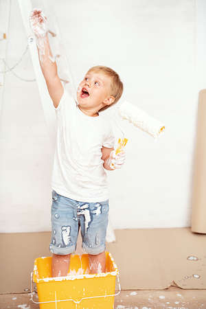 Happy kids painting wall. Home improvement and renovation. Child applying white paint on walls in bedroom. Family moving into new house.の写真素材