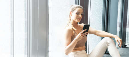 Woman in the gym after workout, using mobile phone.