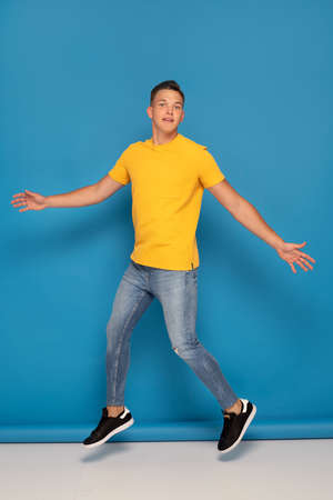 Young handsome man in jeans jumping on blue studio background.