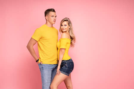 Beautiful young couple smiling, posing on pink pastel studio background.