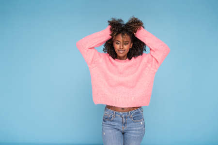 Happy smiling afro girl in pink sweater posing on blue studio background.