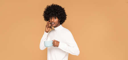 Afro guy holding coffee cup and talking by mobile phone.