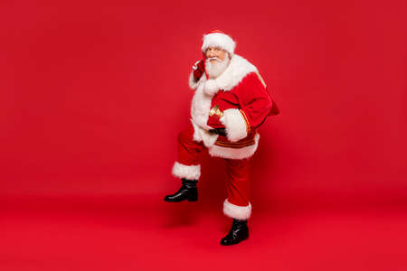 Happy, real, funny Santa Claus holding sack bag with Merry Christmas presents, delivering xmas gifts. Red background, a lot of copy space.の写真素材