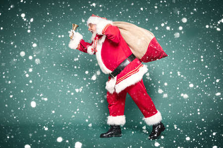 Full length photo of the real, good old Santa Claus carrying gifts in a big sack. Green studio background.の写真素材