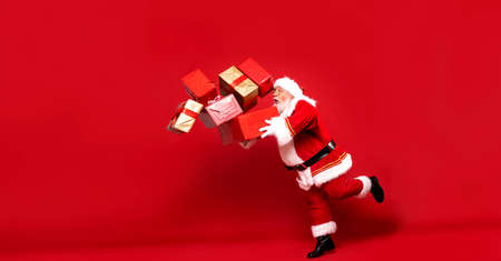 Full length photo of real Santa Claus with a lot of gifts on a red background. Merry Christmas and...