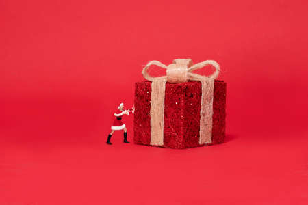 Winter holidays. Girl Santa Claus is pushing large christmas gift box. Red studio background with a...