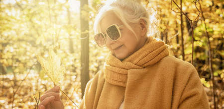 Senior Woman relaxing in autumn golden park, holding leaves in hand. Fall activities.