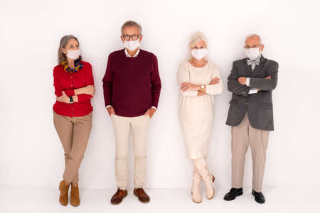 Full length photo of group of senior people posing with face mask covered on the white studio...