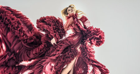 Fashion photo of sensual blonde woman in a long ruffled dress flying in the studio, jumping. A lot of copy space. Elegant style,の写真素材