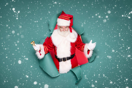 Photo of traditional Santa Claus ringing on a gold bell. Christmas concept.Green studio background. Snow.の写真素材