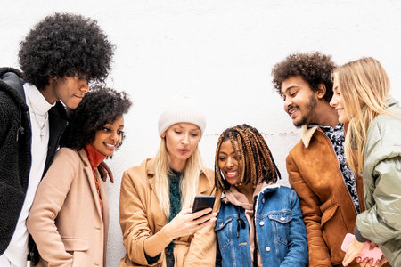 Group of young multiethnic friends looking at mobile phone and watching funny video on social media....