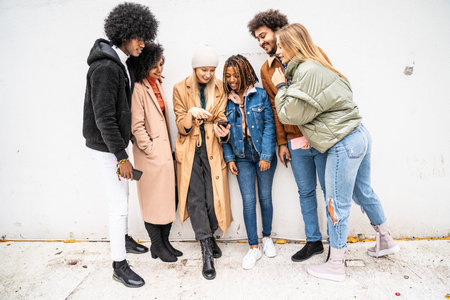 Fashionable multiethnic friends having fun together outdoors, looking at mobile phone. Group of people watching video on the smartphone.の写真素材