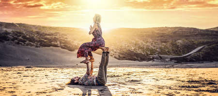 Acro yoga on the beach. Couple meditating and exercising on the sand by the sea at sunset romantic...