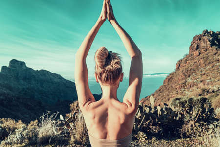 Young woman doing yoga, pilates exercise outdoor in beautiful mountains. Healthy lifestyle and meditation Concept. Wild landscape. Back view.の写真素材