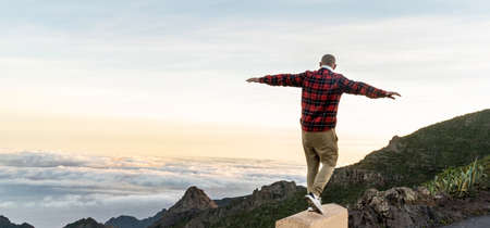 Man Traveler on mountain summit enjoying aerial view hands raised over clouds. Freedom.の写真素材