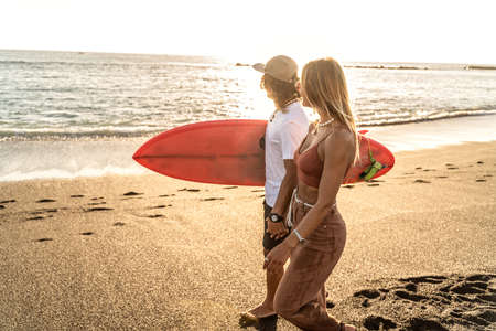 Beautiful young couple walking on the sandy beach during sunset and looking at the ocean. Man...