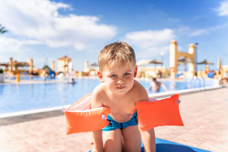 Kid with inflatable armbands near swimming pool. Little boy learning to swim in outdoor pool of tropical resort. Summer vacation.の写真素材