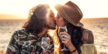 Fashionable boho couple with wine having romantic date on sunset beach, kissing, spending time together. Real people emotions and love concept.の写真素材
