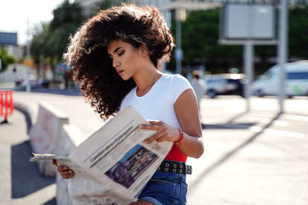 Photo of young colombian woman with afro hairstyle reading newspaper on the city street.の写真素材