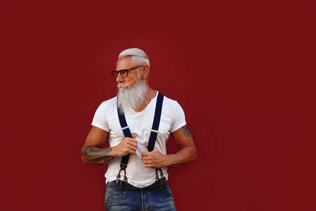 Stylish, fashionable senior man with gray beard and mustache wearing suspenders and eyeglasses,...