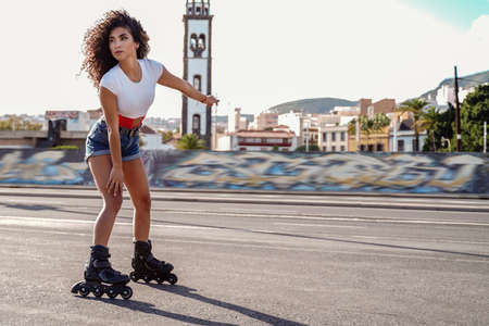 Beautiful young afro woman roller skating on the city street. Cheerful girl on roller skates. Active and healthy lifestyle concept.の写真素材