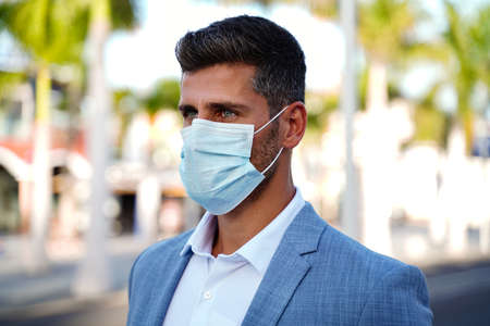 Portrait of handsome man wearing medical blue mask on the face during virus epidemic lockdown. Businessman on the street.の写真素材
