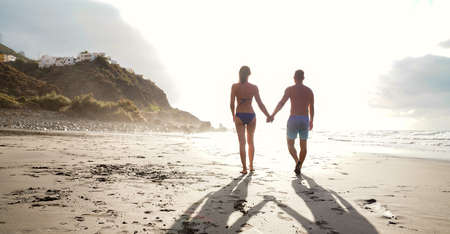 Happy beautiful couple walking together on the beach, holding hands. Summer positive vibes. Sunny vacation day.の写真素材
