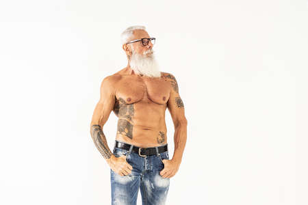 Happy muscular senior man showing his muscular body and tattoos while posing in studio over gray background. Age is just a number. A lot of copy space.の写真素材