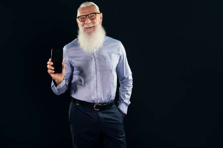 Pleased elderly handsome senior businessman with white beard holding mobile phone with blank empty...