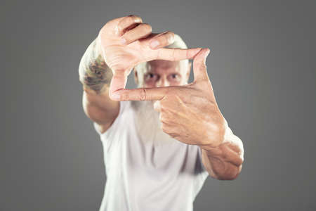 Man framing face with hands on a gray studio background, looking at camera.