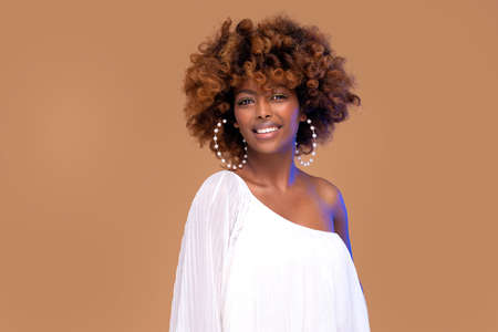 Elegant beautiful girl with toothy smile and afro hairstyle wearing pearl earrings, looking at...