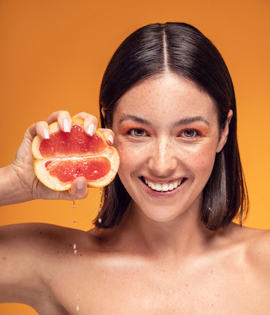 Natural smiling girl with fresh grapefruit. Beauty model squeezing juicy fruit. Joyful woman with natural freckles on face. Concept of a healthy skin care, cosmetology.の写真素材