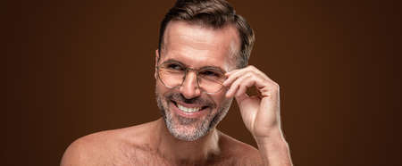 Beauty portrait of handsome man wearing eyeglasses with a toothy smile on his face isolated over brown studio background.の写真素材