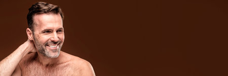 Beauty portrait of handsome caucasian adult man with toothy smile and natural wrinkles. Studio brown background.の写真素材