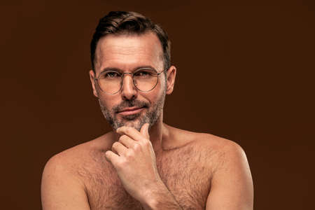 Beauty portrait of handsome man wearing eyeglasses, looking at the camera, isolated over brown studio background.の写真素材