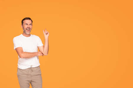 Handsome happy man smiling and looking at the camera, pointing with his finger at empty place, isolated on yellow studio background. A lot of copy space for your text.の写真素材