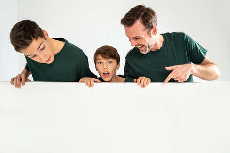 Dad and his two sons pointing on an empty white board, smiling. Studio shot. Real people emotions....