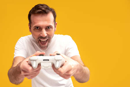 Gambling addiction. Excited mature man holding joystick and playing video games, looking at the...