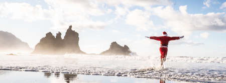 Merry Christmas and a Happy New Year! Funny conceptual photo of Santa Claus jumping like a super hero on a tropical beach at the ocean.の写真素材