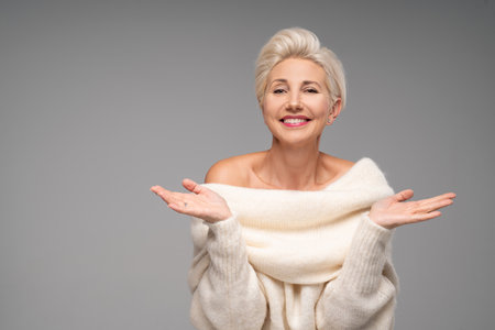 Beauty portrait of smiling adult blonde woman with short hairstyle and glamor makeup. Attractive lady wearing warm fashionable sweater. A lot of copy space. Studio shot.の写真素材