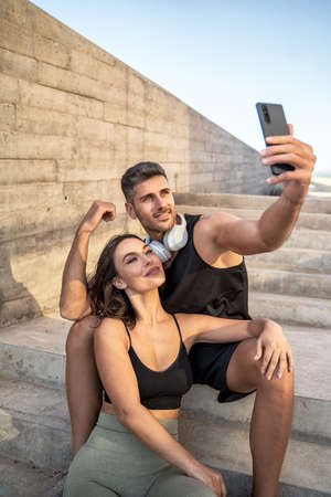 Attractive happy couple taking a selfie with a smartphone after outdoor workout. Sport and healthy...