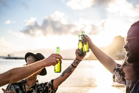 Group of happy young multi ethnic people having fun together on the beach. Smiling friends raising a toast with beer. Summer sunset time. Multiracial girls and guys drinking, partying, Students lifestyle. Real people emotions.の写真素材