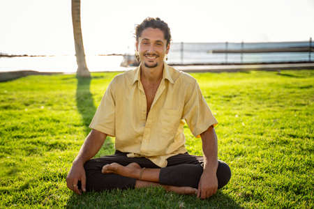 Smiling hippie italian man sitting in lotus, practicing yoga outdoor on sunny day. Men looking at the camera with cute smile. A lot of copy space.の写真素材