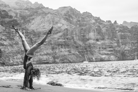 Young fitness woman doing handstand exercise on the rocky beach, practicing yoga on seashore. Morning routine. Tenerife. Los Gigantes.の写真素材