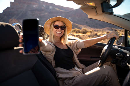 Happy smiling blonde woman in summer hat and sunglasses wearing comfortable clothes driving cabrio...