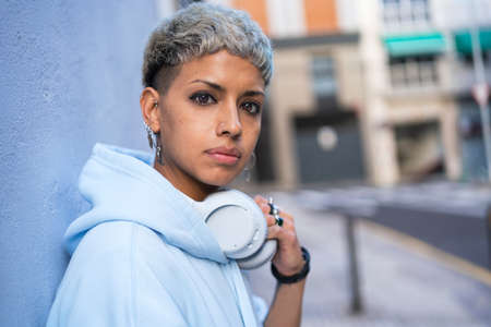 Young beautiful woman with short haircut posing with white headphones, looking at the camera. Real...